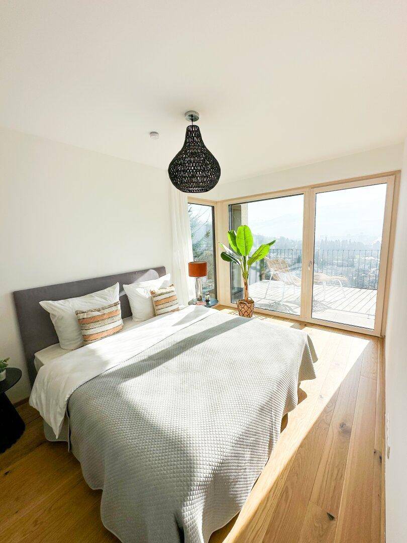 Helles Schlafzimmer mit Holzboden, modernem Bett und Panoramablick durch große Fenster.