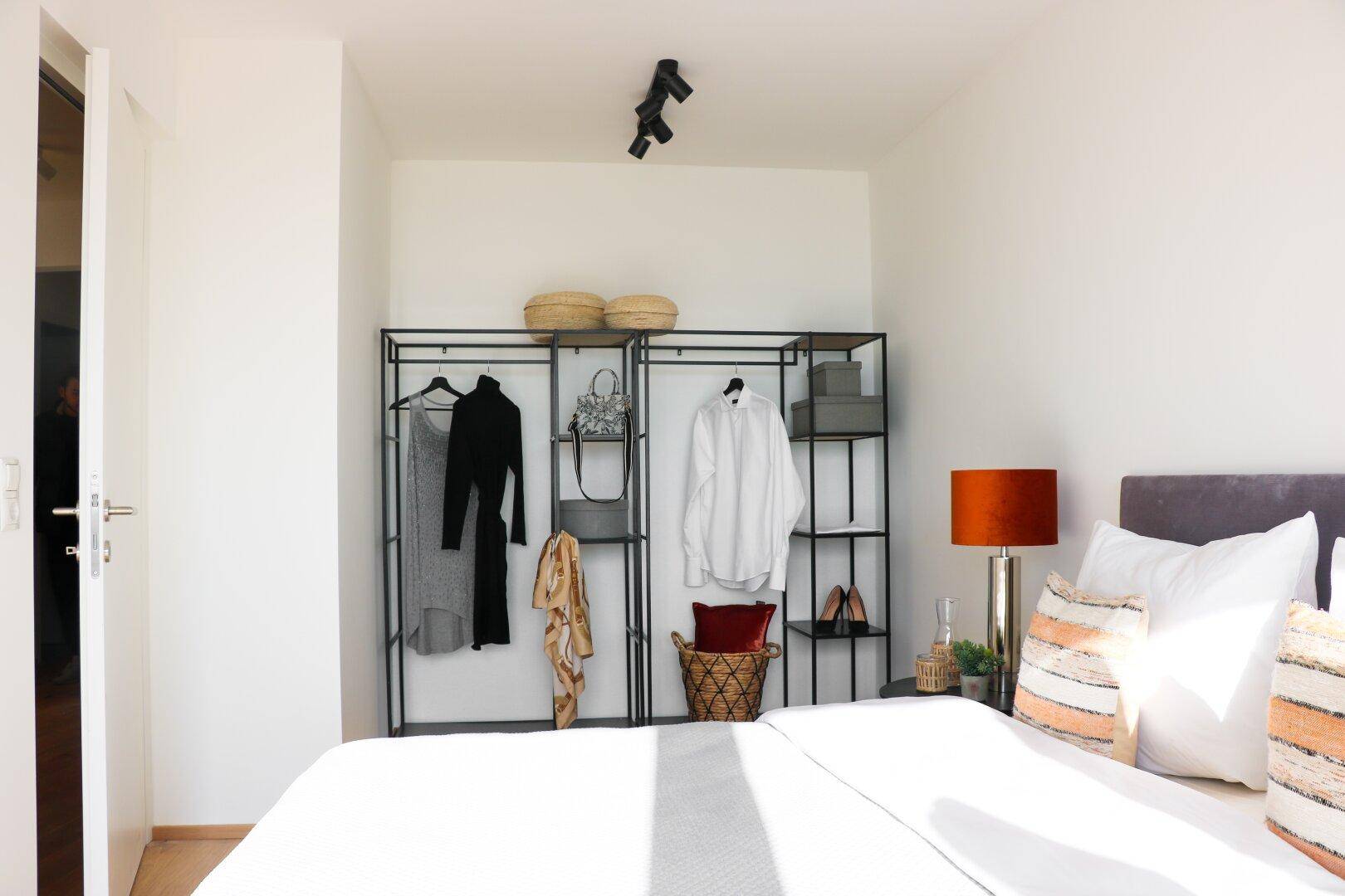 Schlafzimmer mit Bett, offenem Kleiderschrank und viel Tageslicht.