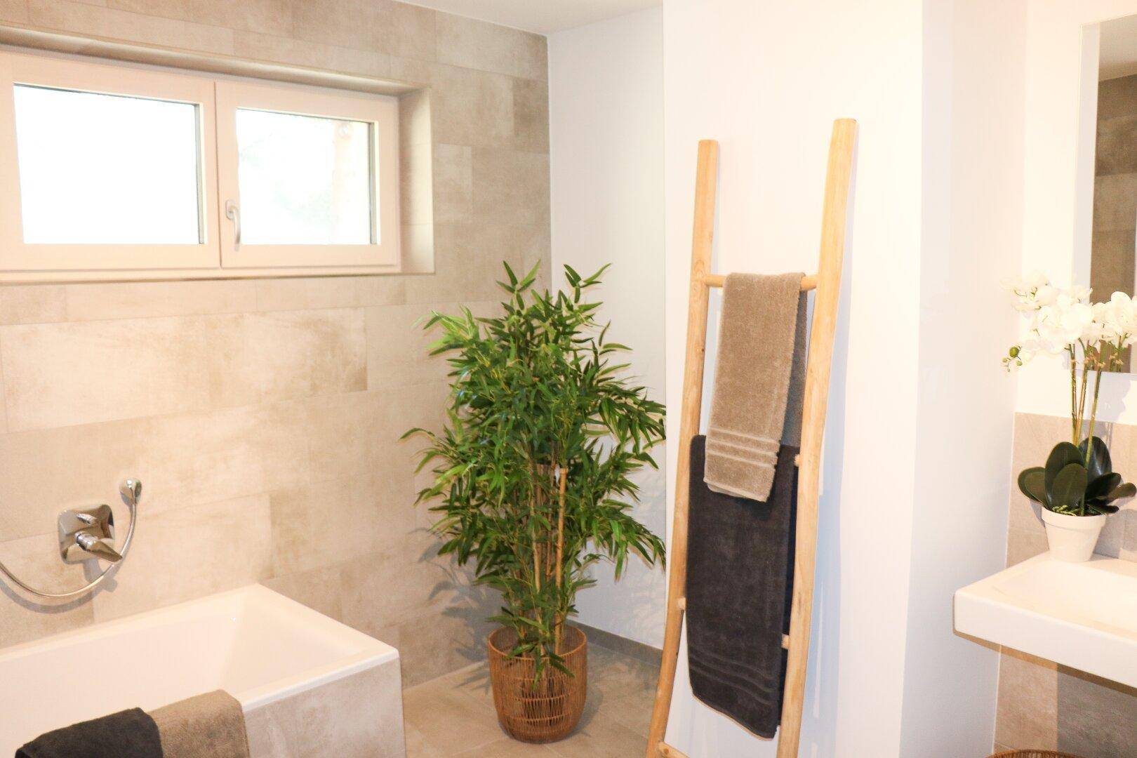 Modernes Badezimmer mit Badewanne, hellen Fliesen und Fenster für Tageslicht.