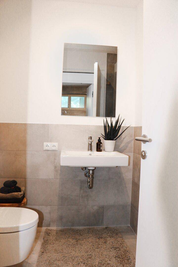 Modernes Gäste-WC mit Waschbecken, Spiegel und hellen Fliesen.
