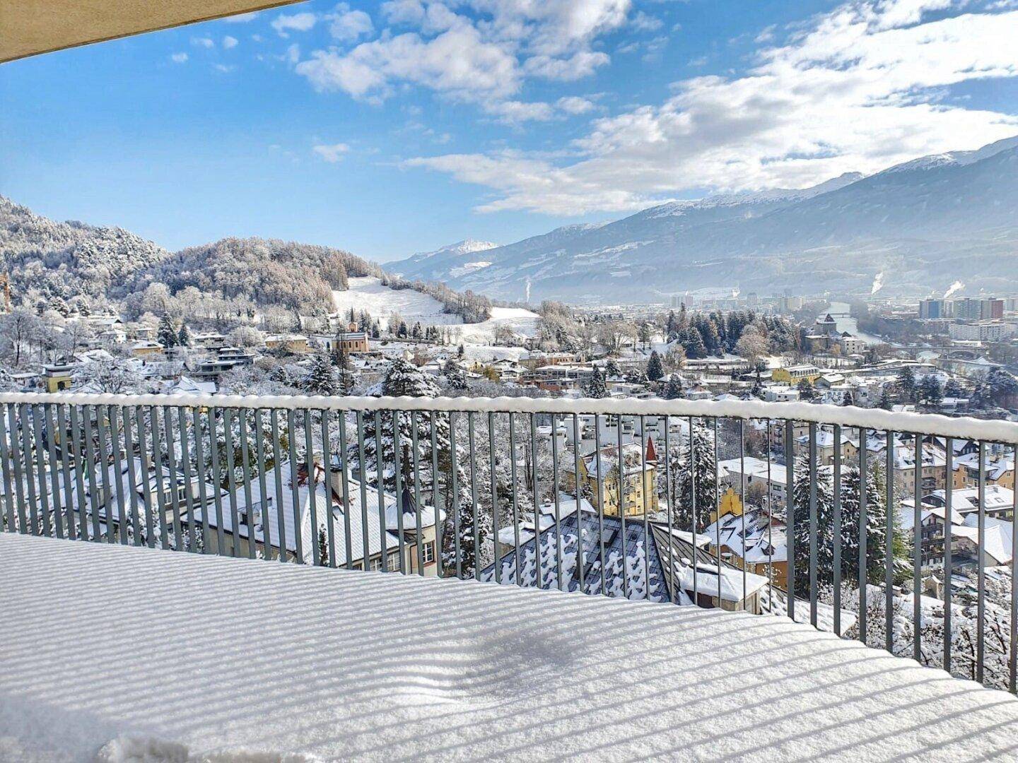 Schneebedeckter Balkon mit malerischem Blick auf die winterliche Stadt und die Berge.