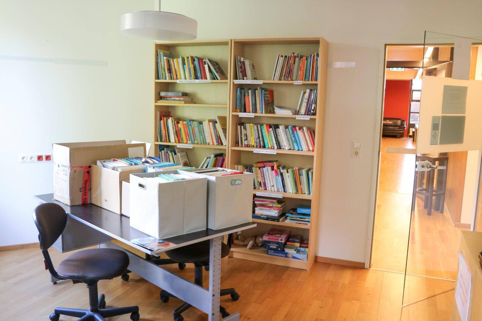 Büroraum mit Bücherregalen, einem Schreibtisch und Blick auf einen weiteren Bereich.
