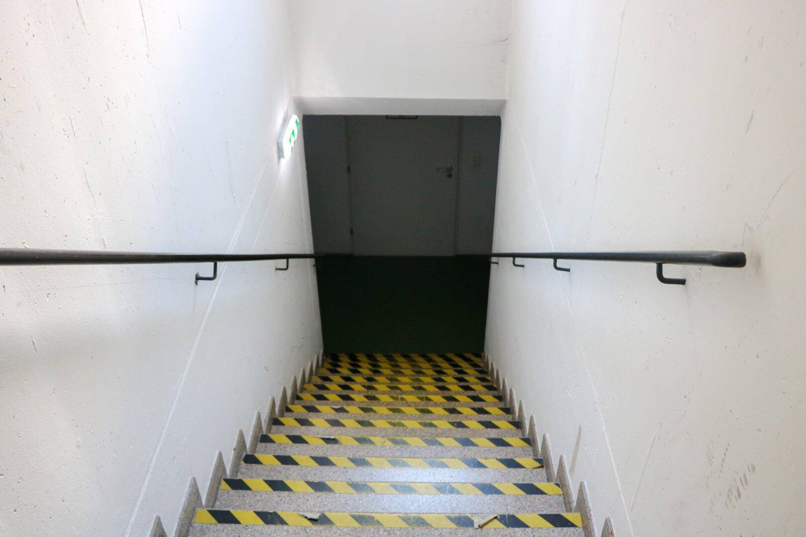 Treppenhaus mit gelb-schwarz gestreiften Stufen und einem schwarzen Handlauf.