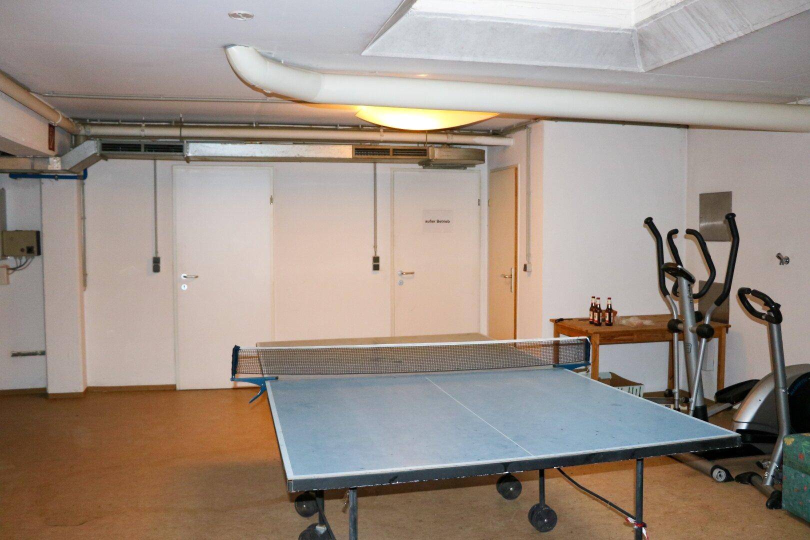 Kellerraum mit Tischtennisplatte, Fitnessgeräten und sichtbaren Rohren an der Decke.