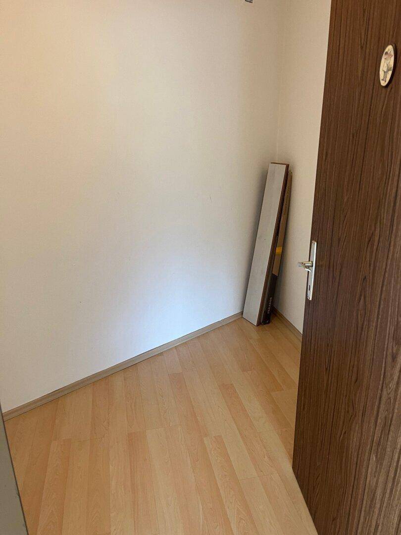 Kleiner, leerer Raum mit hellem Laminatboden und einer Holztür, möglicherweise ein Abstellraum.