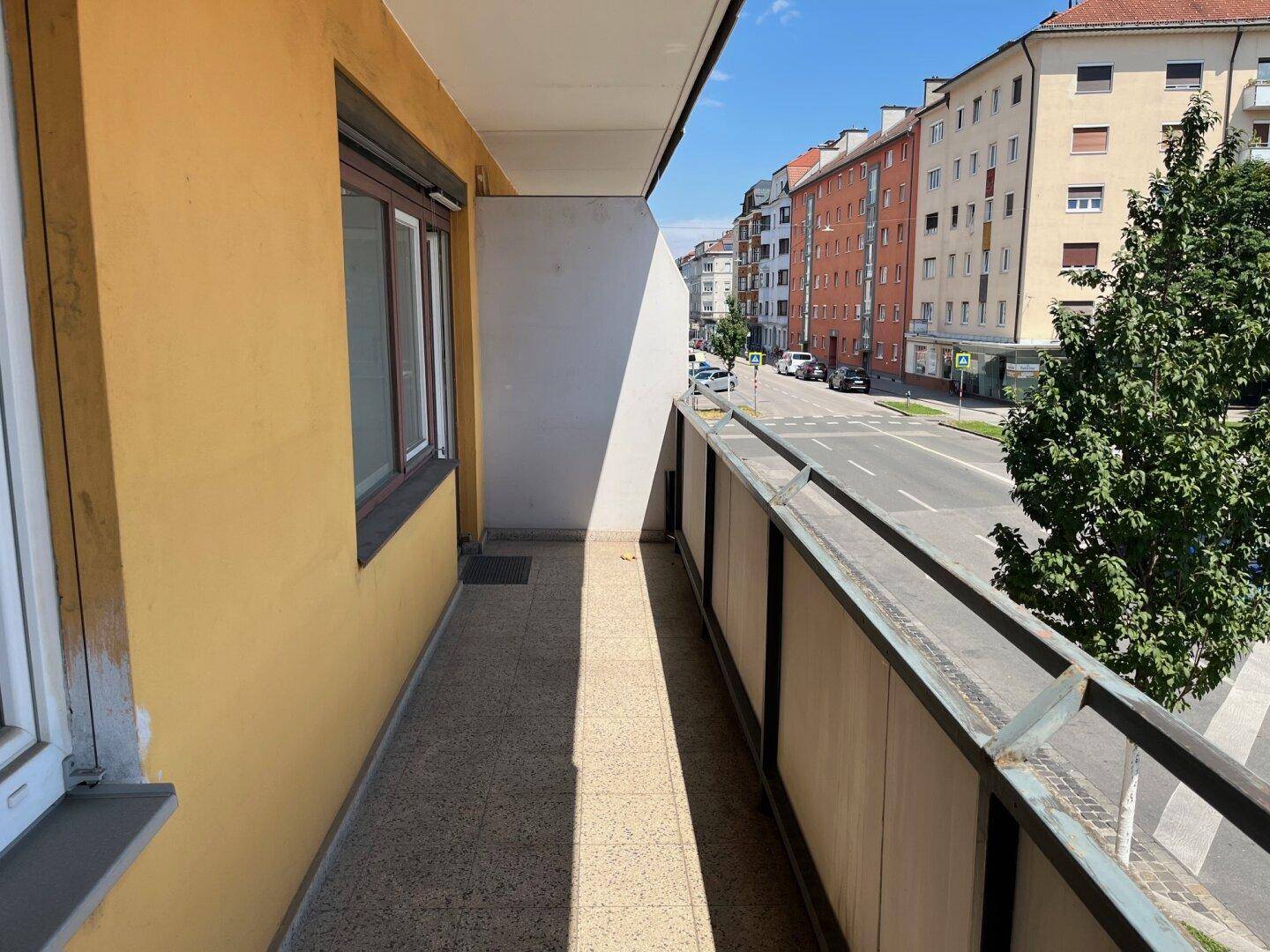 Langer Balkon mit gelber Fassade und Blick auf die Straße und die gegenüberliegenden Gebäude.