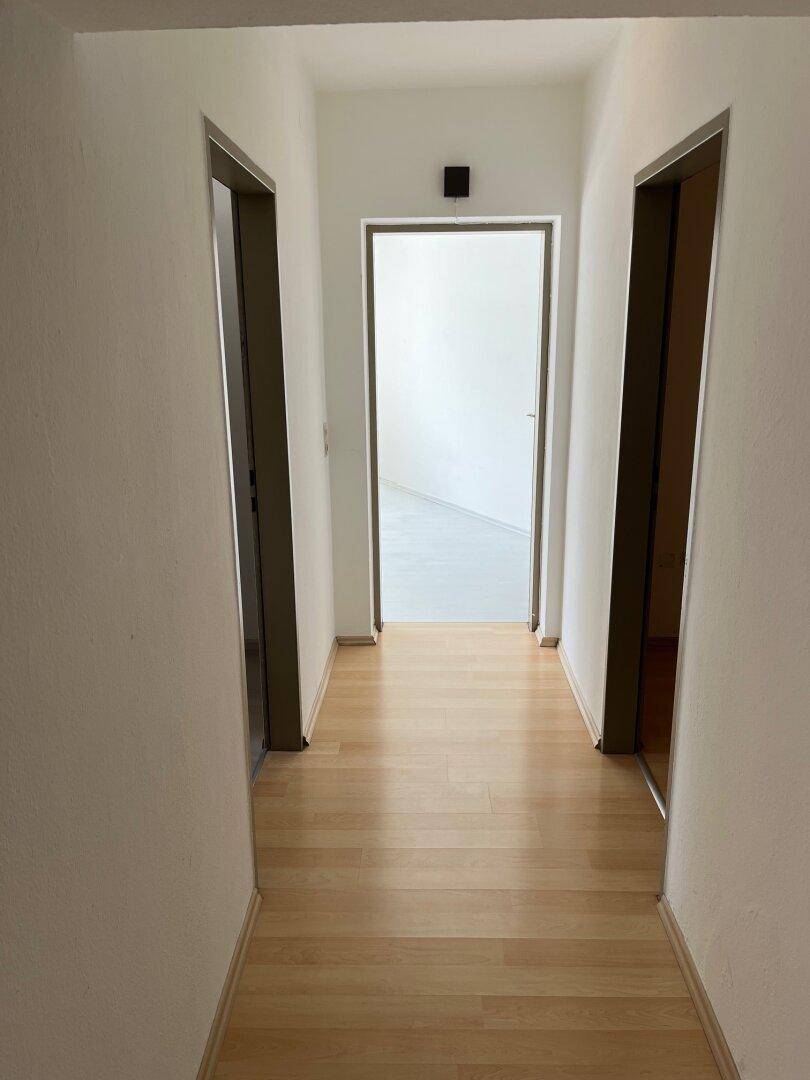 Langer, schmaler Flur mit hellem Laminatboden und weißen Wänden, der zu mehreren Türen führt.