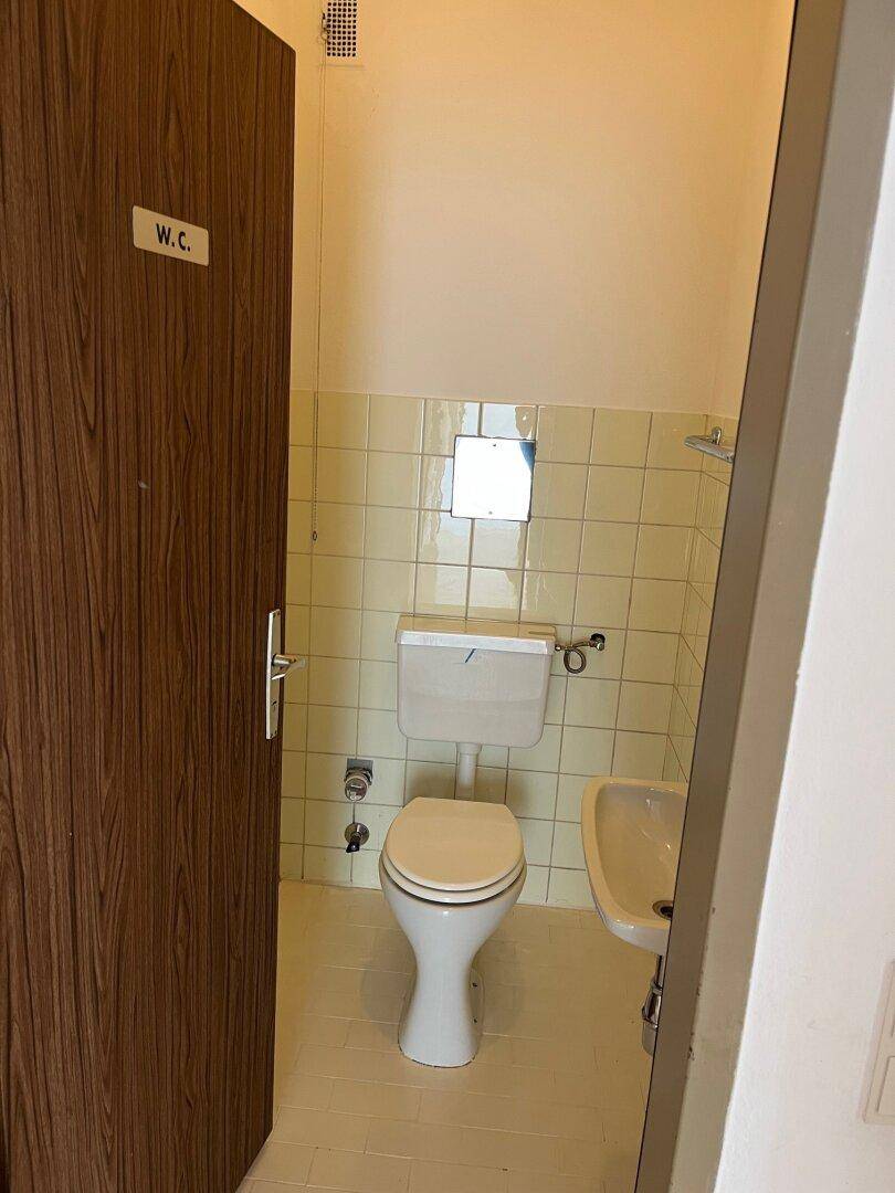 Separate Toilette mit beigefarbenen Fliesen, WC und kleinem Handwaschbecken.