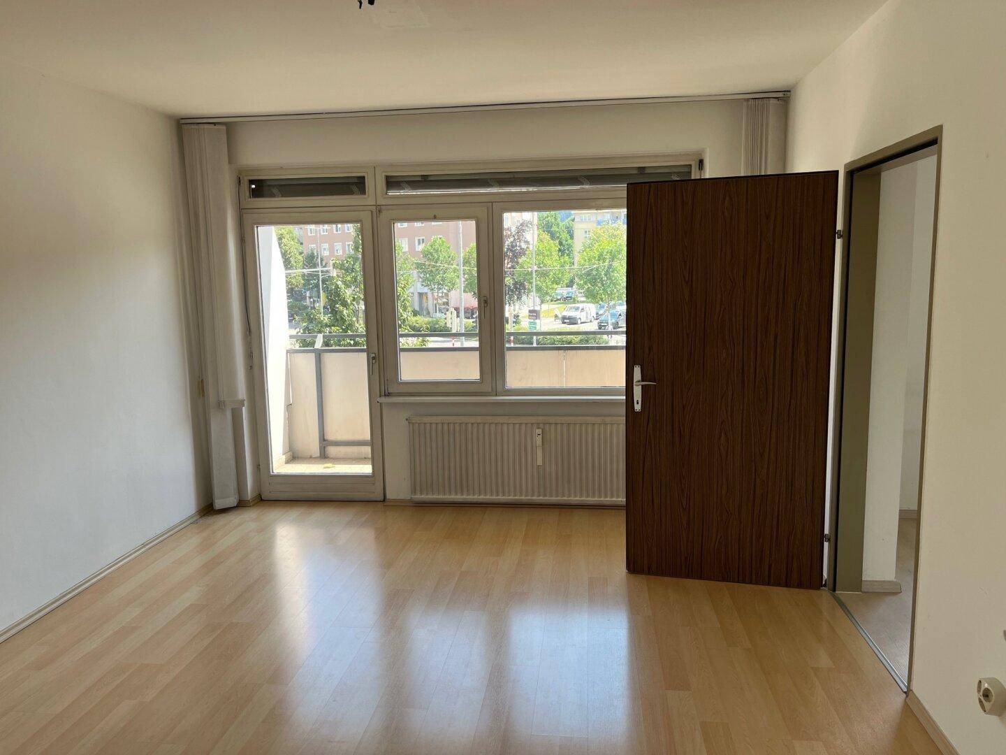 Helles Zimmer mit Laminatboden und Zugang zu einem Balkon, ideal als Wohn- oder Schlafzimmer.