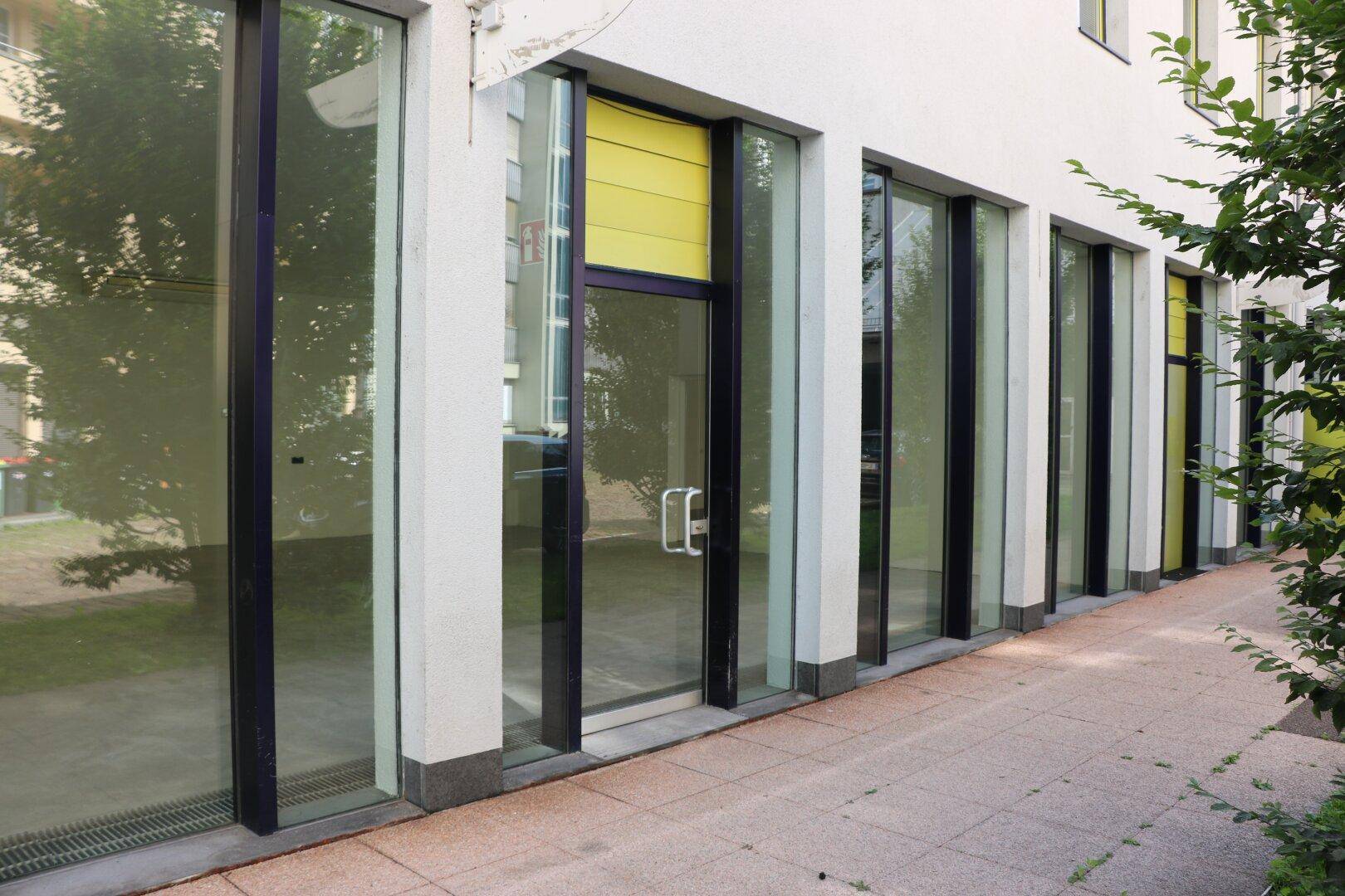 Seitenansicht der modernen Gebäudefassade mit durchgehenden Glasfenstern und einem gelben Rollladen.