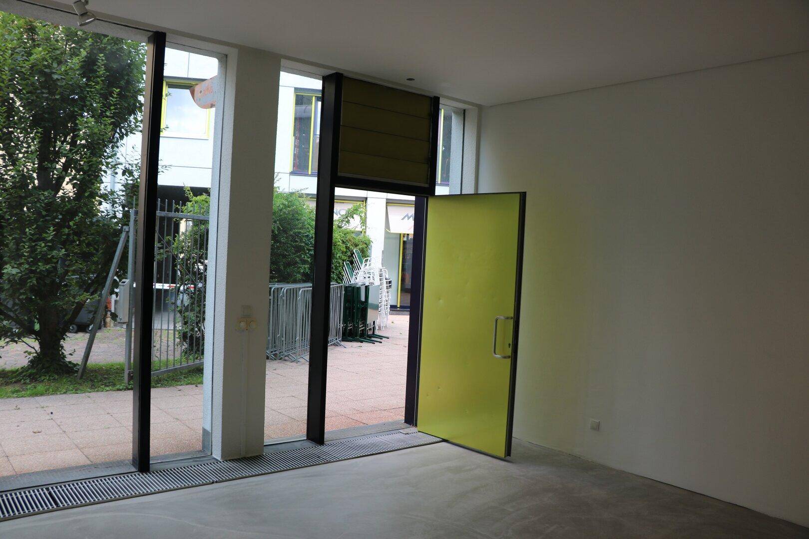 Heller Gewerberaum mit großen Fenstern und einer gelben Tür, die nach draußen führt.