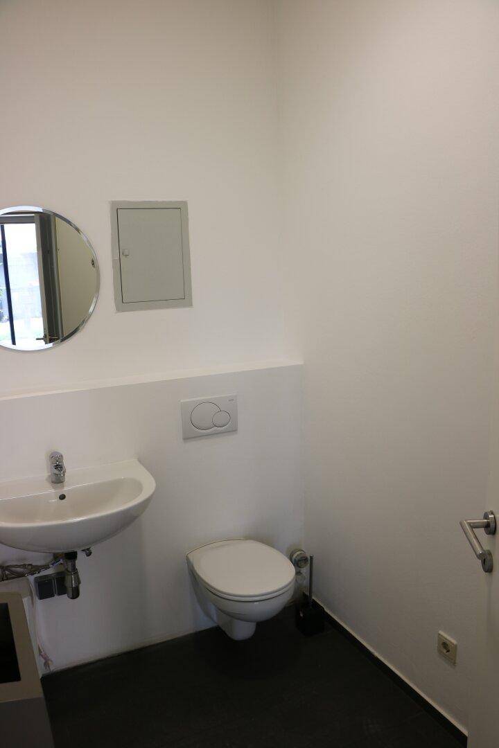 Saubere und moderne Toilette mit Wand-WC, Waschbecken und rundem Spiegel.
