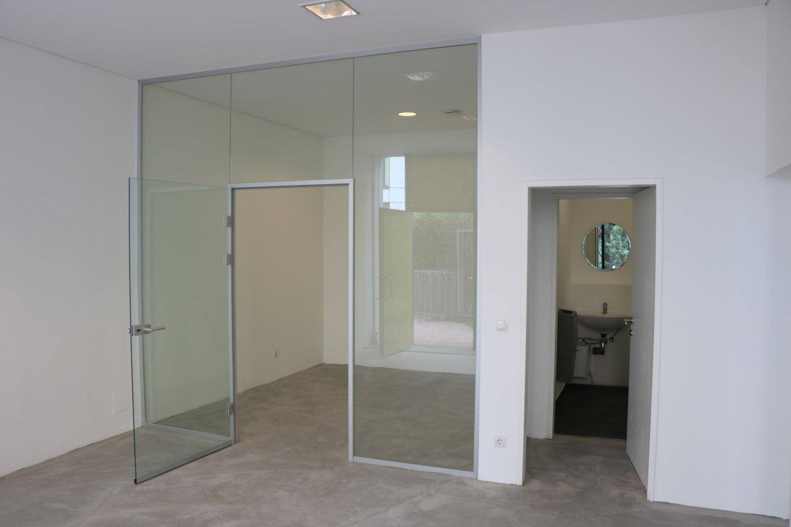 Heller, leerer Gewerberaum mit modernen Glaswänden und Zugang zu einer Toilette.