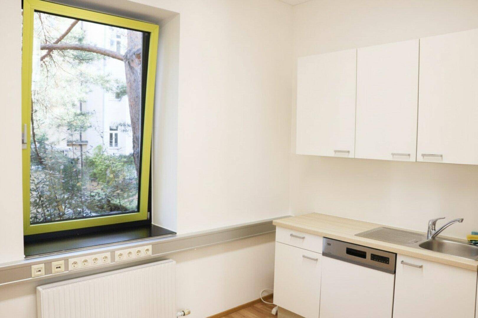 Küchenzeile mit weißen Schränken, Holztheke und Fenster mit Blick auf Bäume.