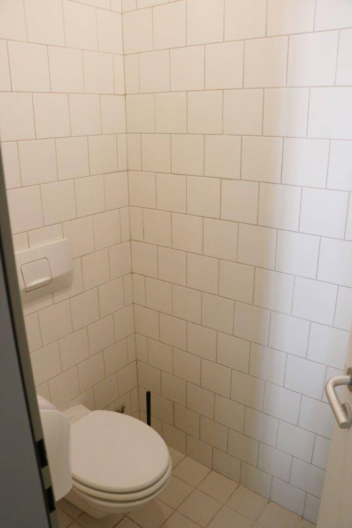 Kleine Toilette mit weißen Fliesen an Wänden und Boden, sowie einer Wandtoilette.