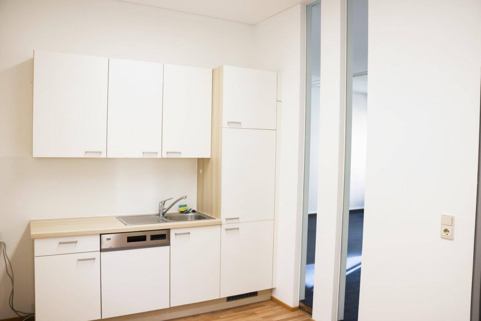 Kleine, moderne Küchenzeile mit weißen Schränken, Holztheke und integriertem Geschirrspüler.