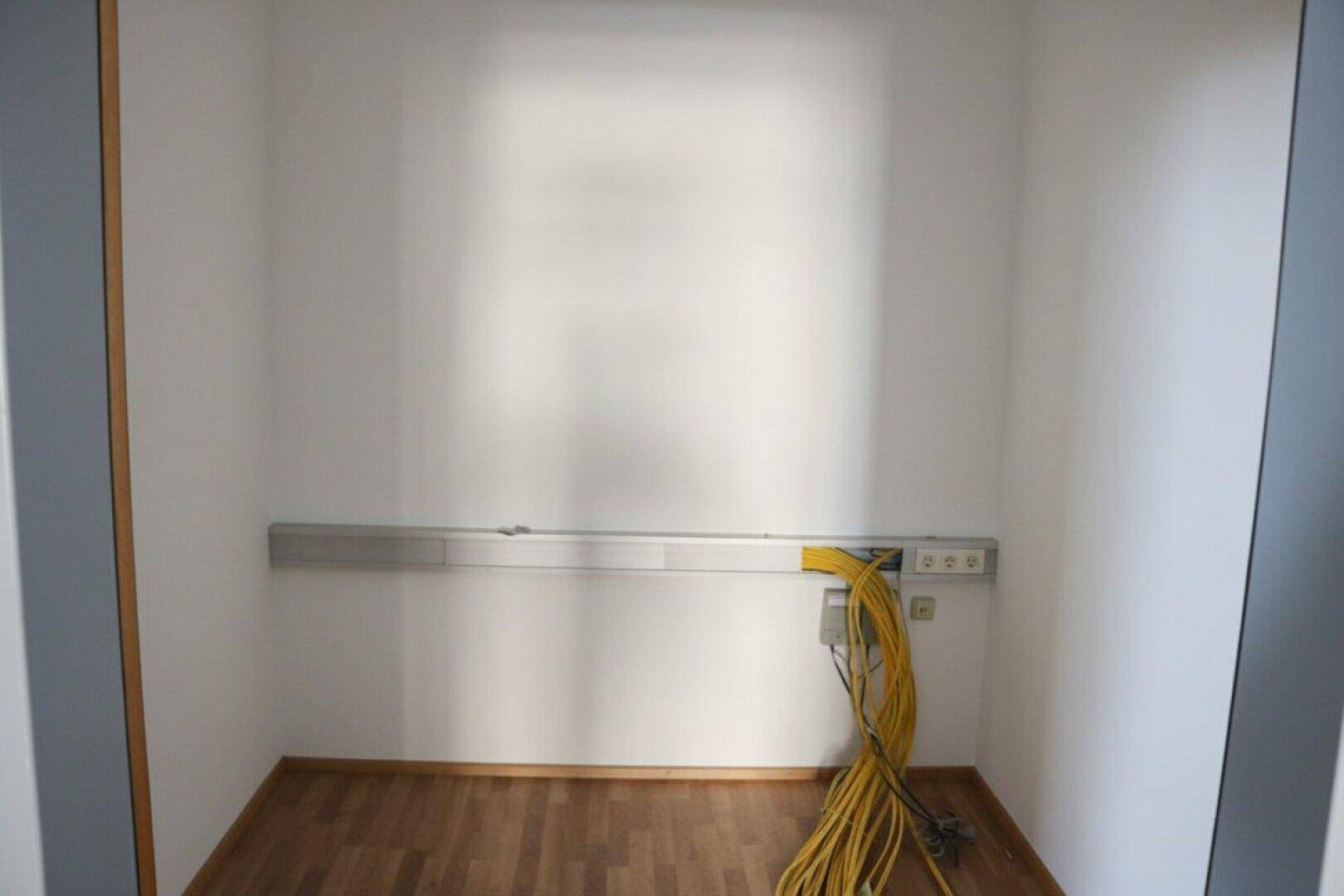 Kleiner Abstellraum mit Holzboden, weißen Wänden und sichtbaren Kabeln an der Wand.