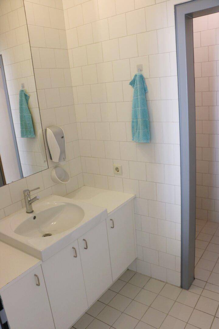Badezimmer mit weiß gefliesten Wänden, Waschbecken, Spiegel und einem Urinal.