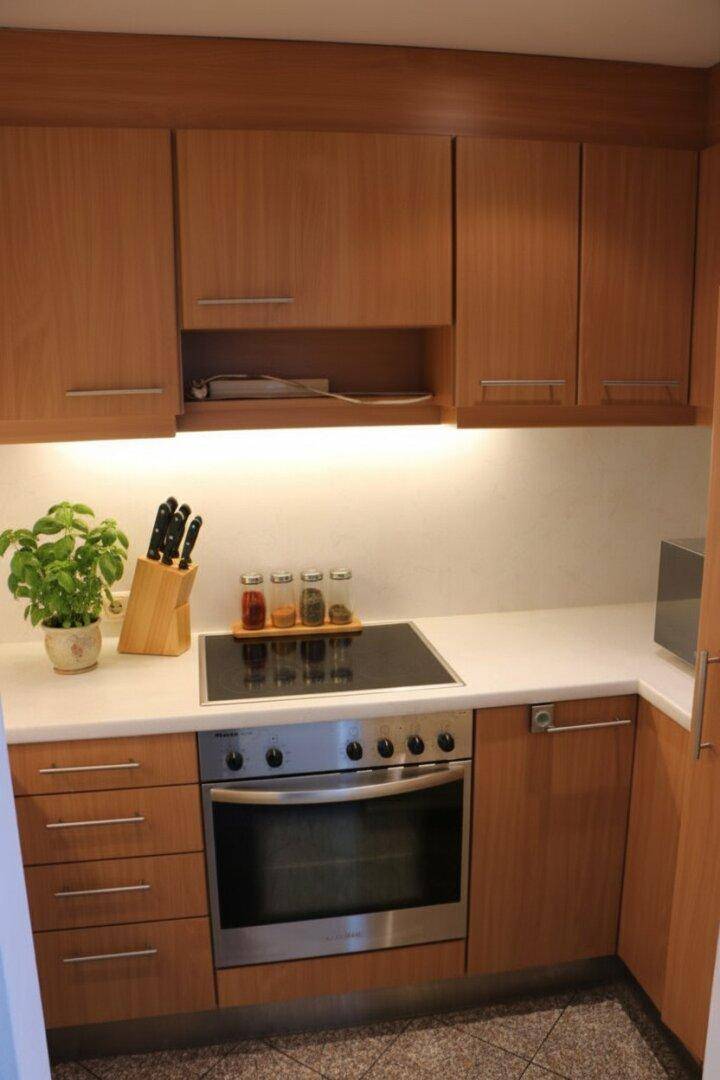Kompakte Küche mit Holzschränken, integriertem Backofen und Kochfeld, ideal für effizientes Kochen.