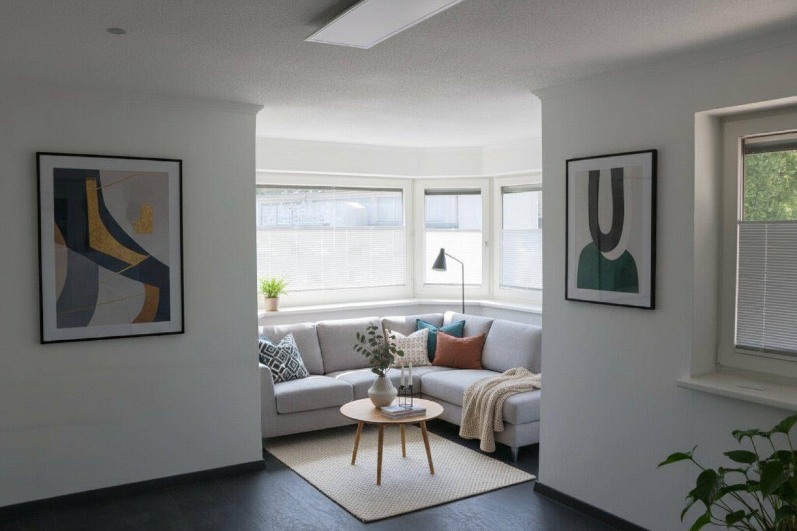 Modern eingerichtetes Wohnzimmer mit Ecksofa, stilvollen Bildern und großen Fenstern für viel Tageslicht.