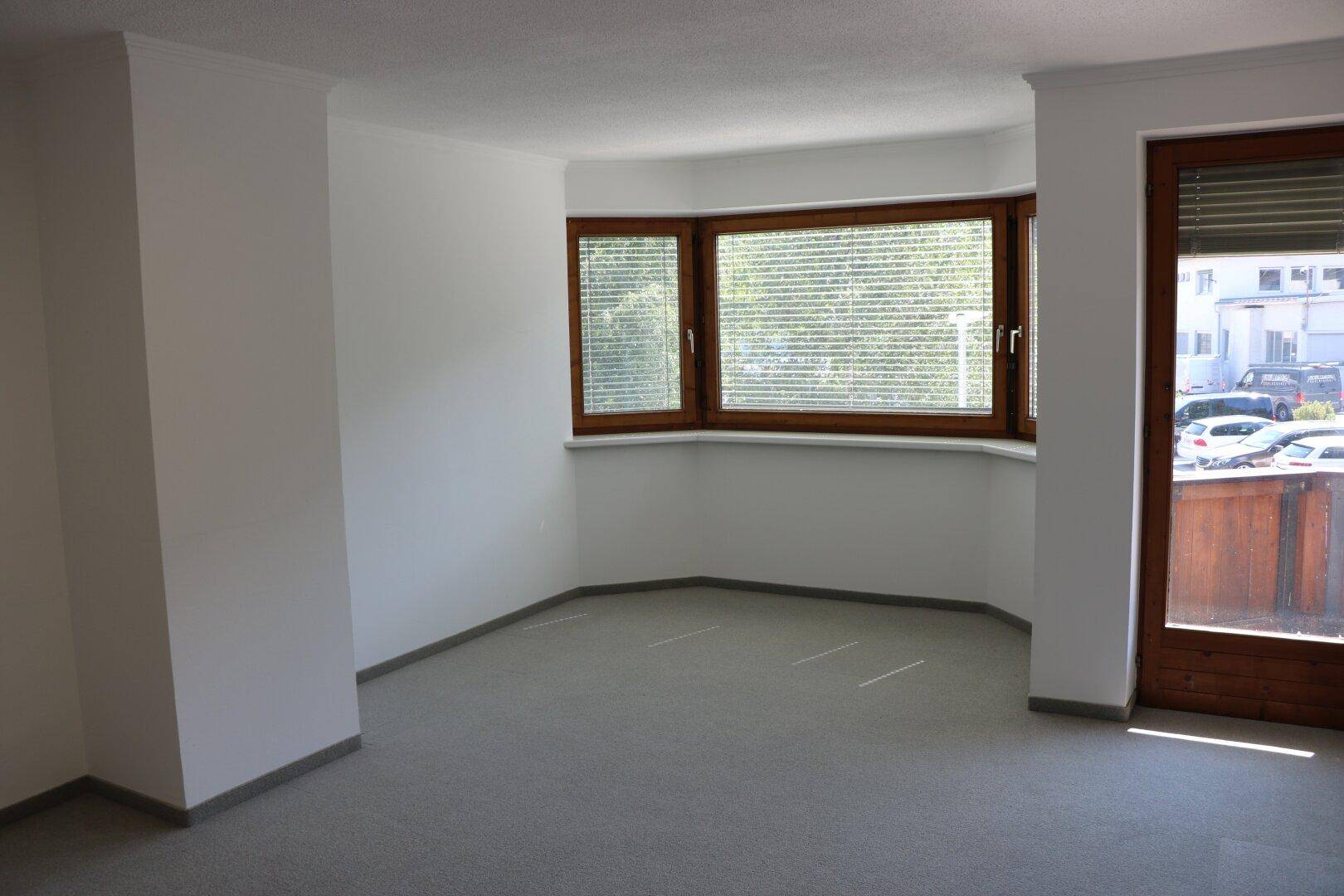 Heller, leerer Raum mit grauem Teppichboden und großen Holzfenstern, bereit zur individuellen Gestaltung.