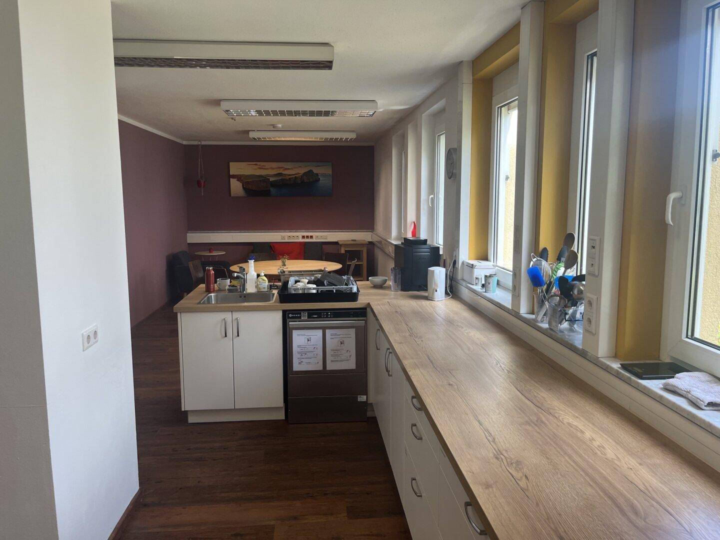 Geräumige Küche mit langer Arbeitsplatte, Spülmaschine und Essbereich im Hintergrund.