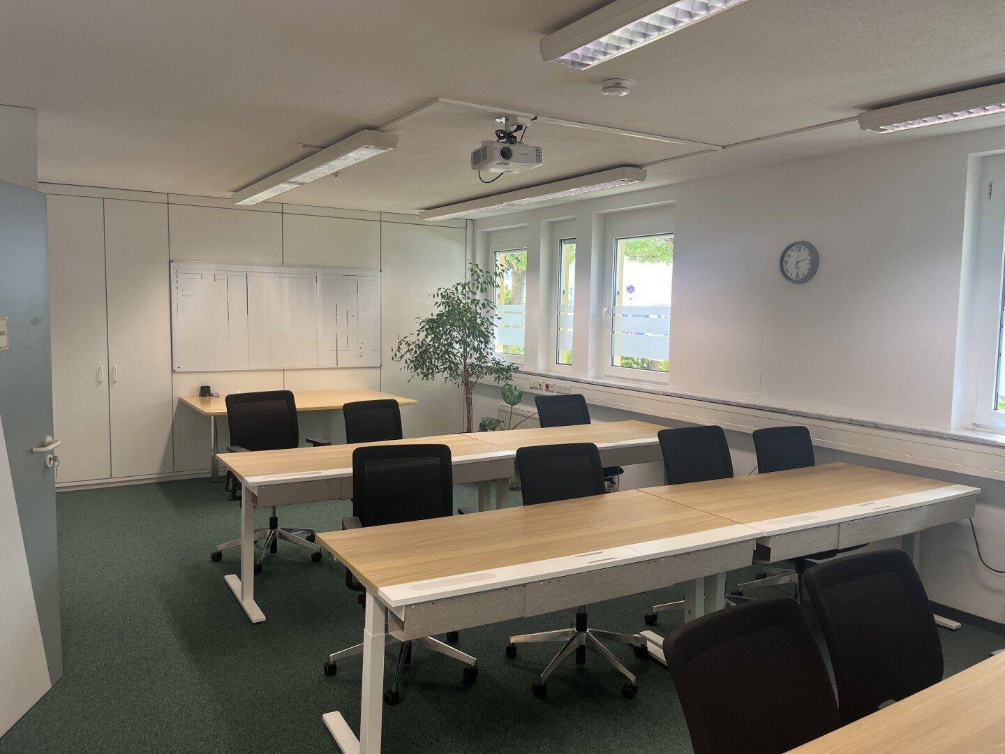 Konferenzraum mit mehreren Tischen, Bürostühlen, Whiteboard und Teppichboden.