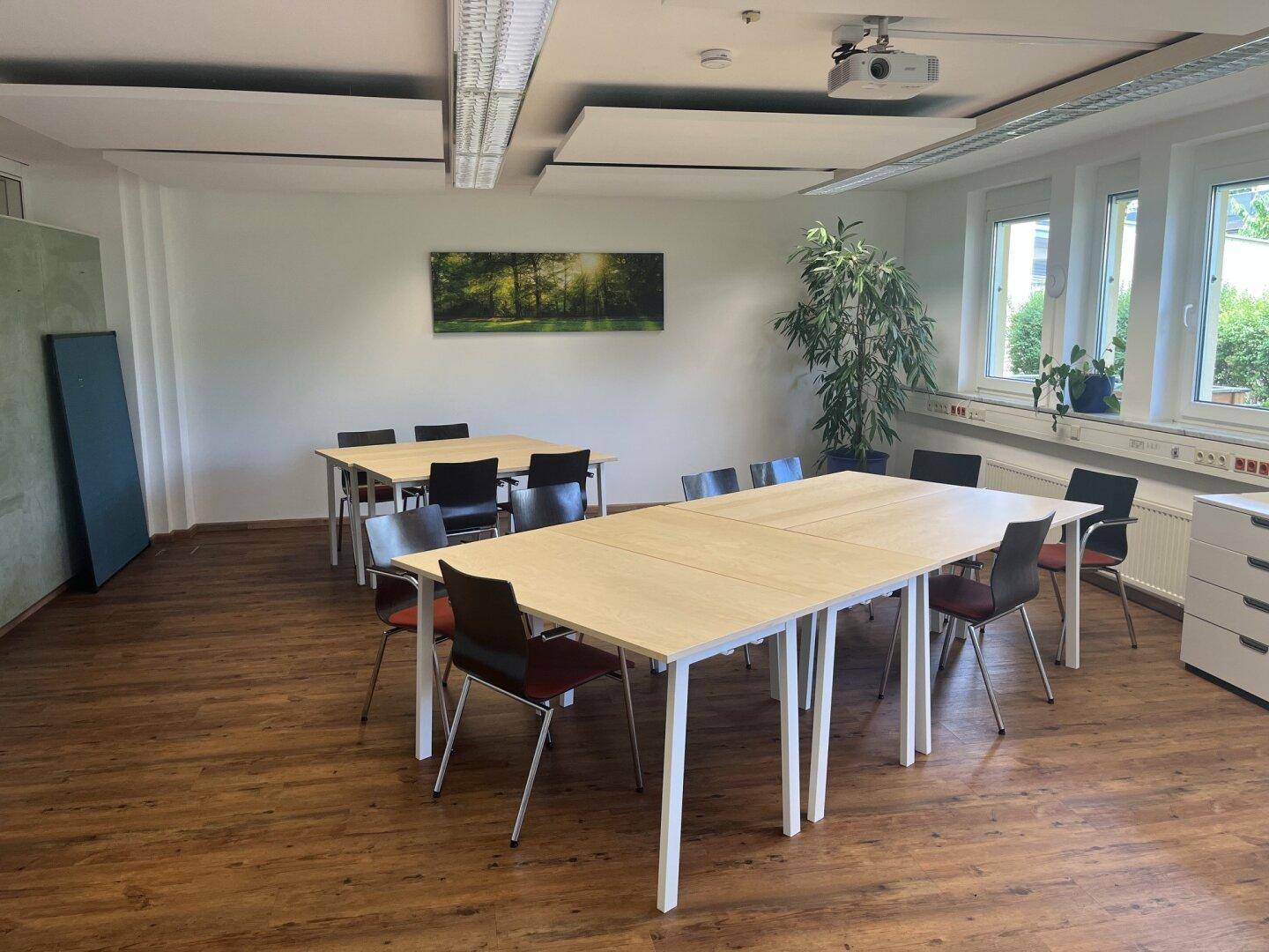 Großer Konferenzraum mit mehreren Tischen, Stühlen und einem Beamer für Präsentationen.