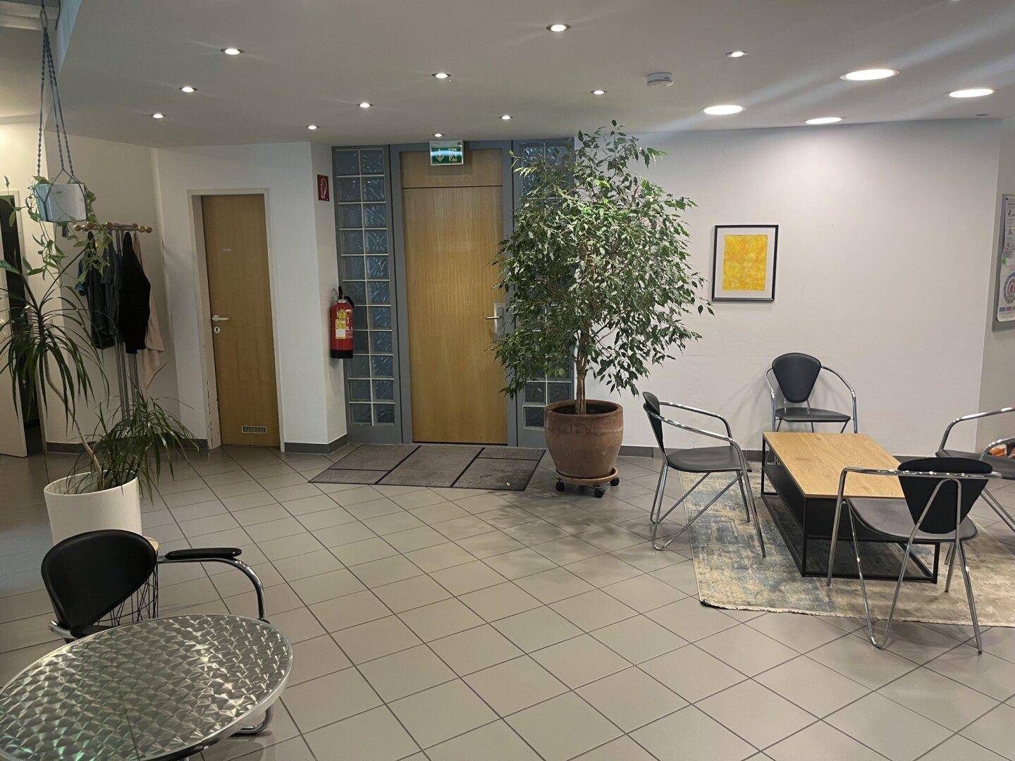 Heller Empfangsbereich mit Fliesenboden, Sitzgelegenheiten und dekorativen Pflanzen.