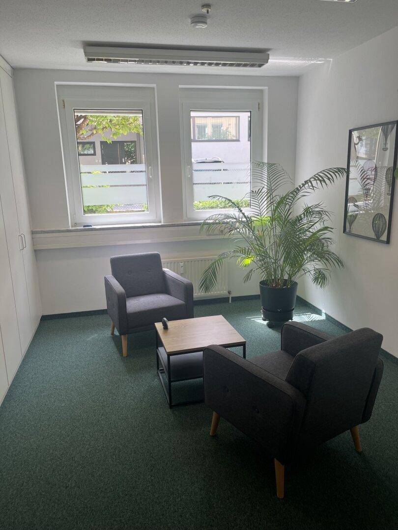 Kleines Büro oder Besprechungszimmer mit zwei Sesseln, einem Couchtisch und Teppichboden.