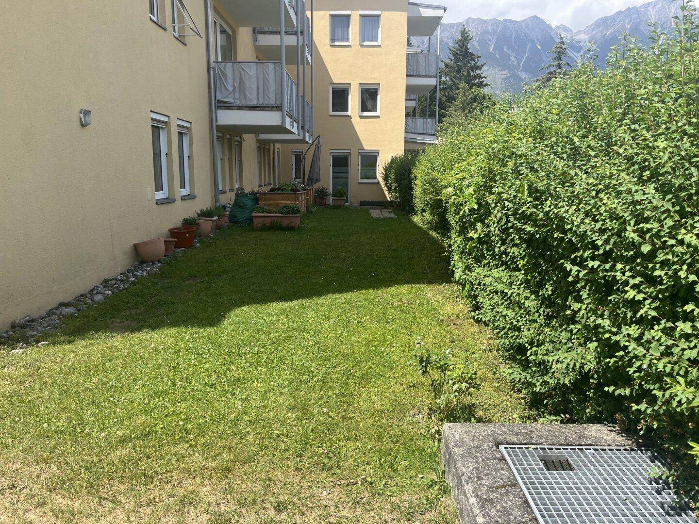 Hinterhof mit Rasenfläche, umgeben von Hecken und Blick auf die Berge im Hintergrund.