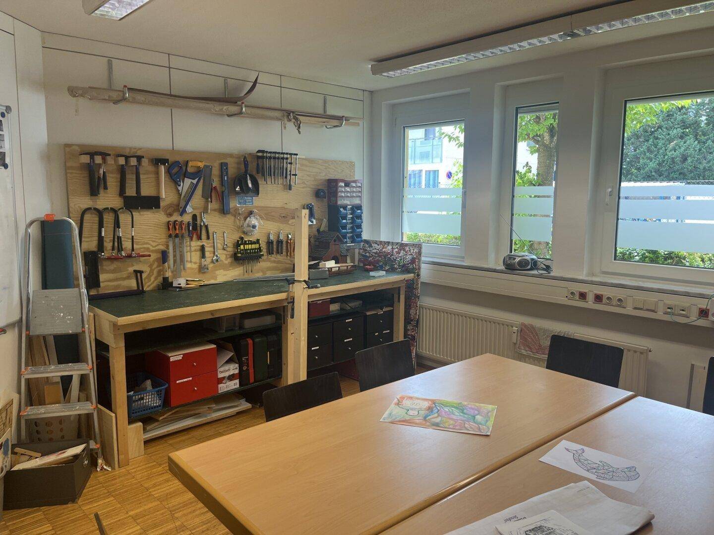 Werkstattbereich mit Werkbank, Werkzeugen an der Wand und einem großen Arbeitstisch.