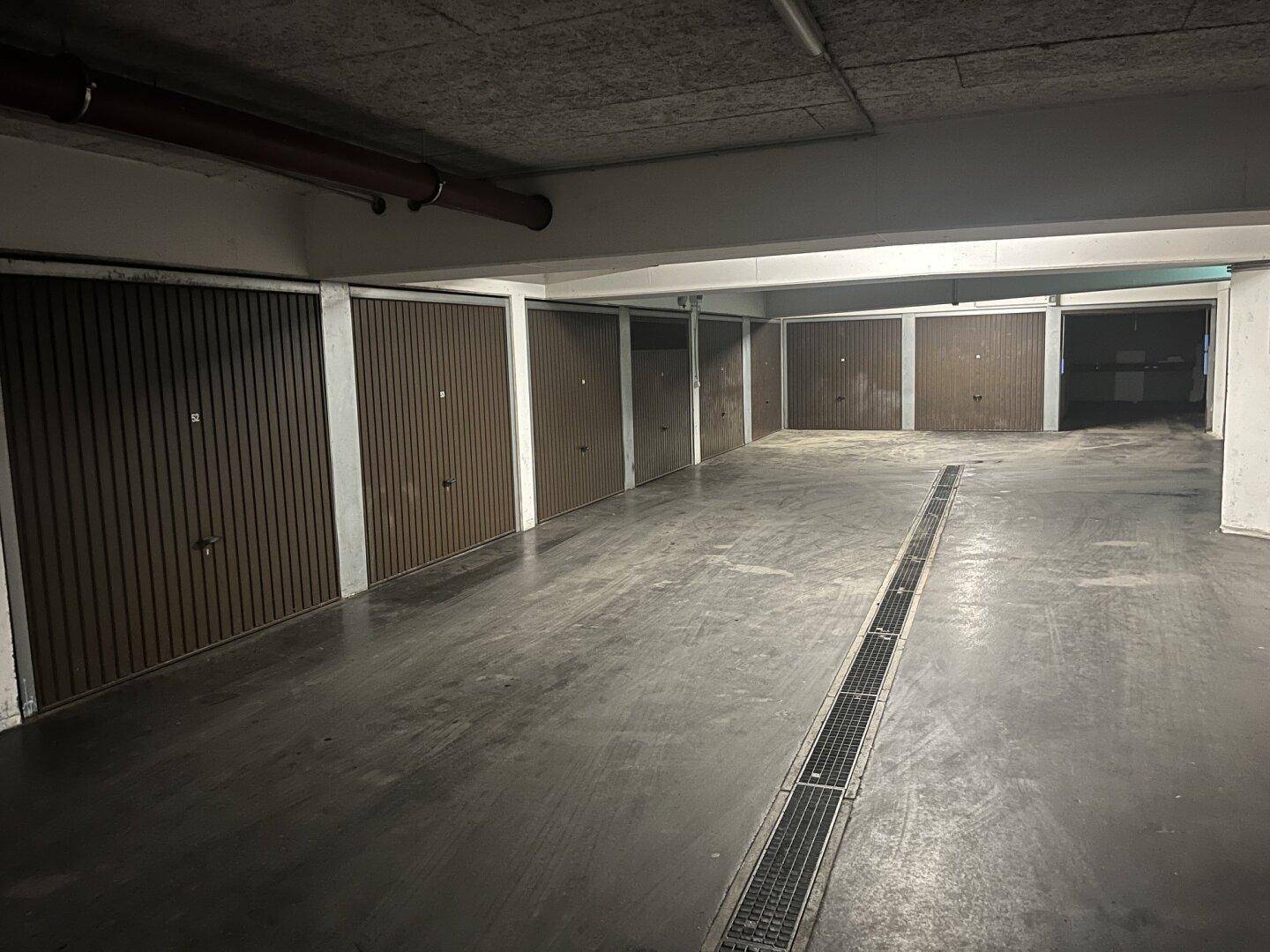 Eine Tiefgarage mit mehreren Garagentoren und Betonboden, gut beleuchtet.