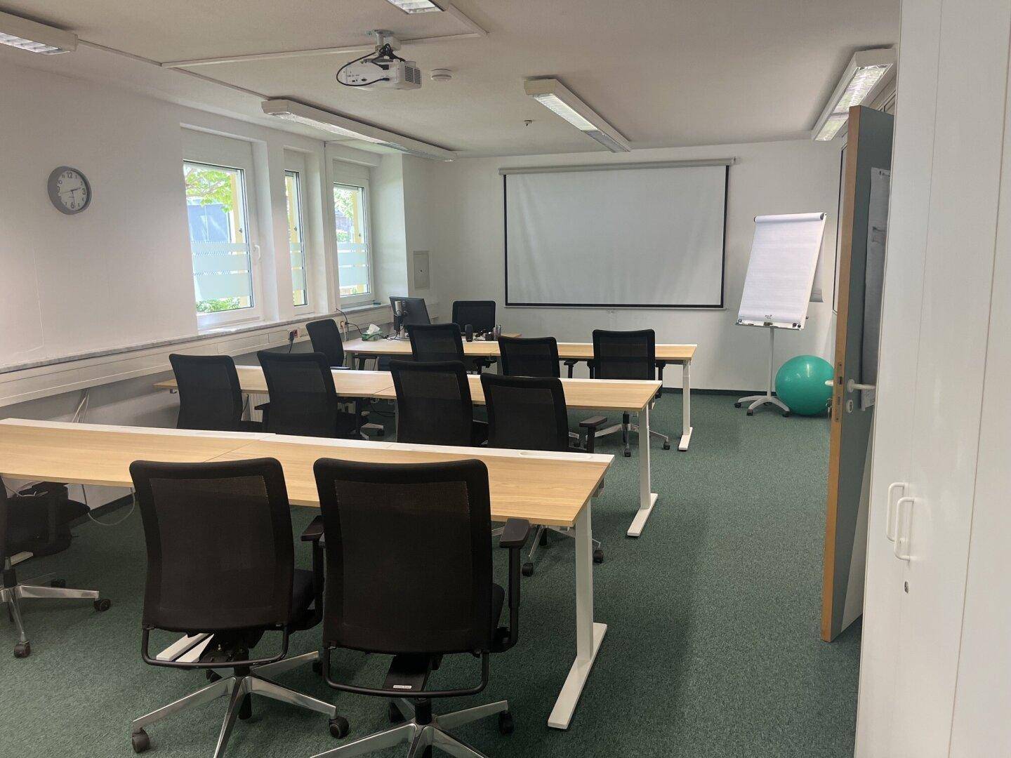 Konferenzraum mit Projektionsfläche, Flipchart und mehreren Tischen und Stühlen.