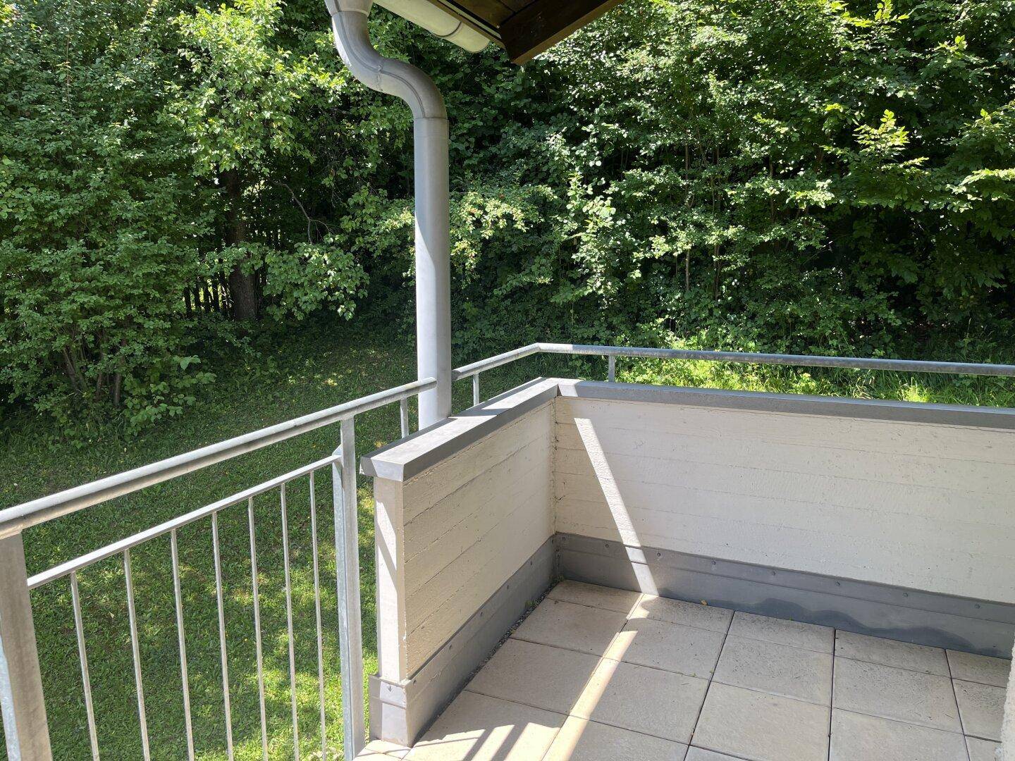 Kleiner Balkon mit Fliesenboden und Metallgeländer, umgeben von grüner Natur.