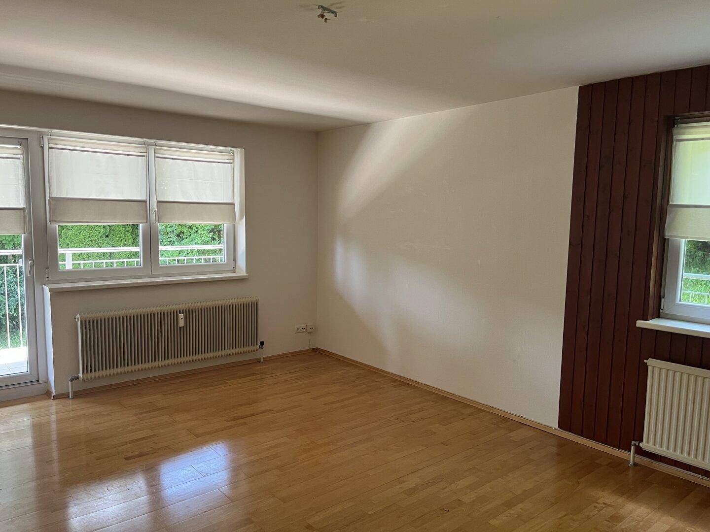 Helles Zimmer mit Holzboden, einer Holzwand und Zugang zu einem Balkon.