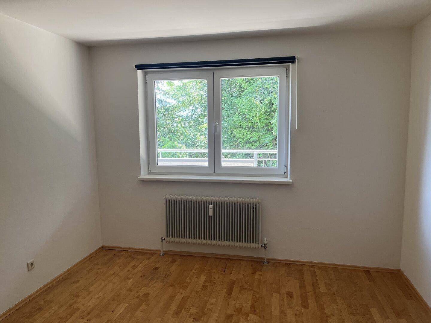 Helles Schlafzimmer mit Holzboden und großem Fenster mit Blick auf Bäume.