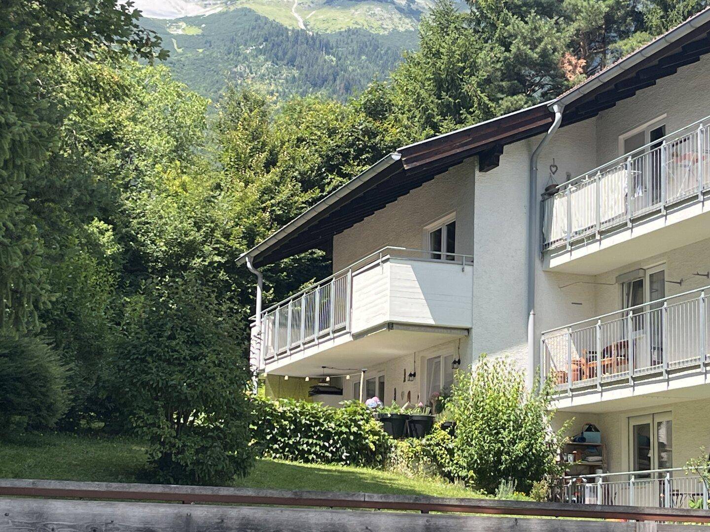 Mehrfamilienhaus mit Balkonen, eingebettet in grüne Natur und mit Bergblick.