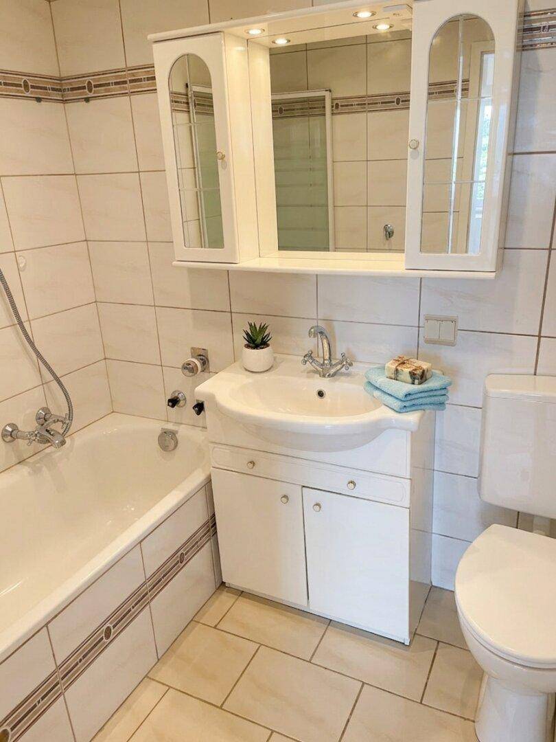Traditionelles Badezimmer mit Badewanne, Waschbecken und Spiegelschrank, komplett gefliest.