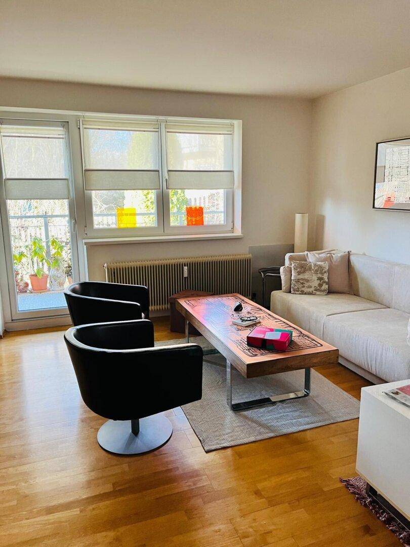Helles Wohnzimmer mit Holzboden, bequemen Sitzmöbeln und Zugang zu einem Außenbereich.