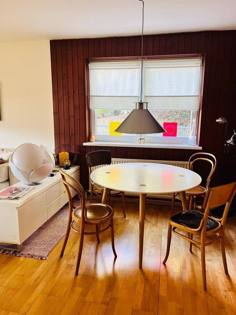 Heller Essbereich mit rundem Tisch, Holzstühlen und einer Wandverkleidung aus dunklem Holz.