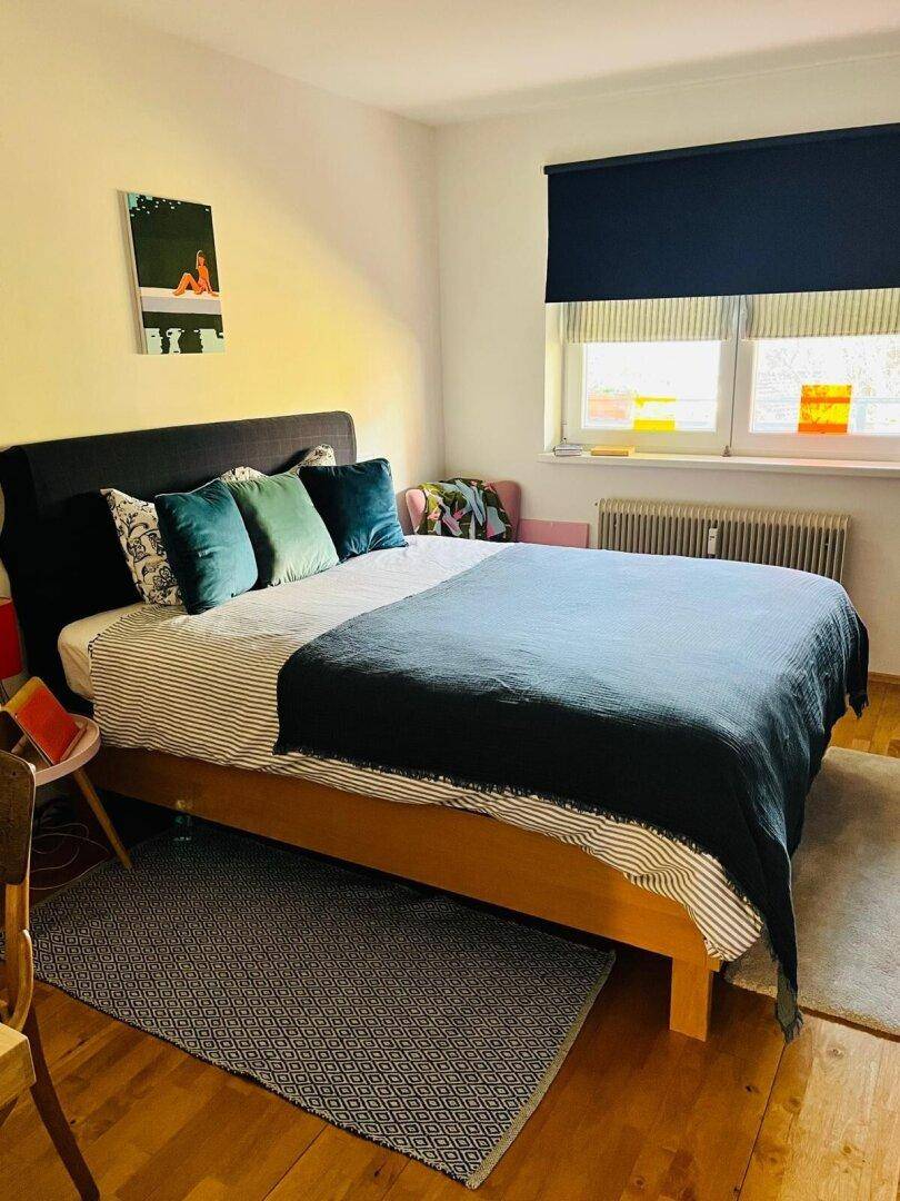 Gemütliches Schlafzimmer mit Holzbett, blauer Bettwäsche und einem Fenster für natürliches Licht.