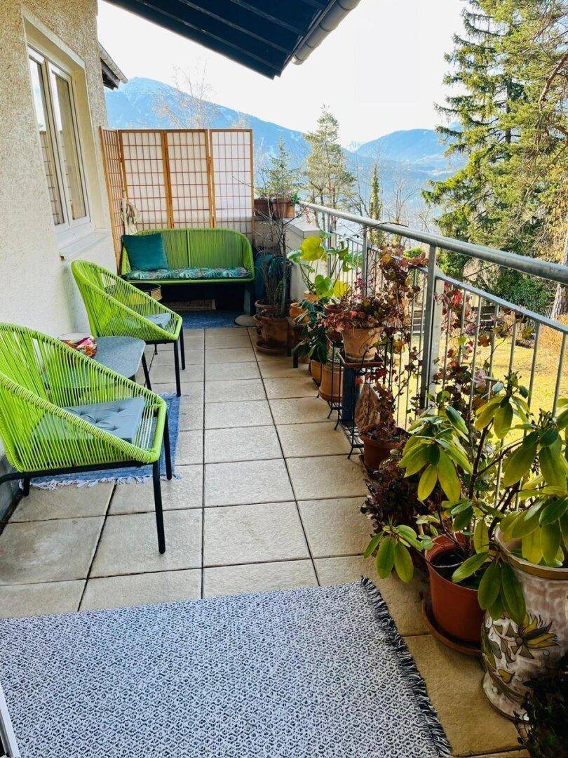 Langer Balkon mit modernen grünen Stühlen, vielen Pflanzen und herrlichem Bergblick.