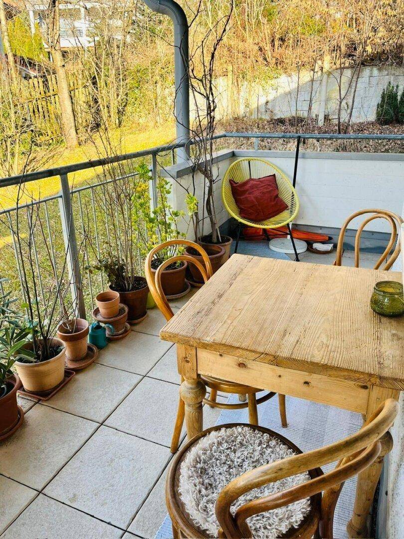 Gemütlicher Balkon mit Holztisch, vielen Pflanzen und Blick ins Grüne.