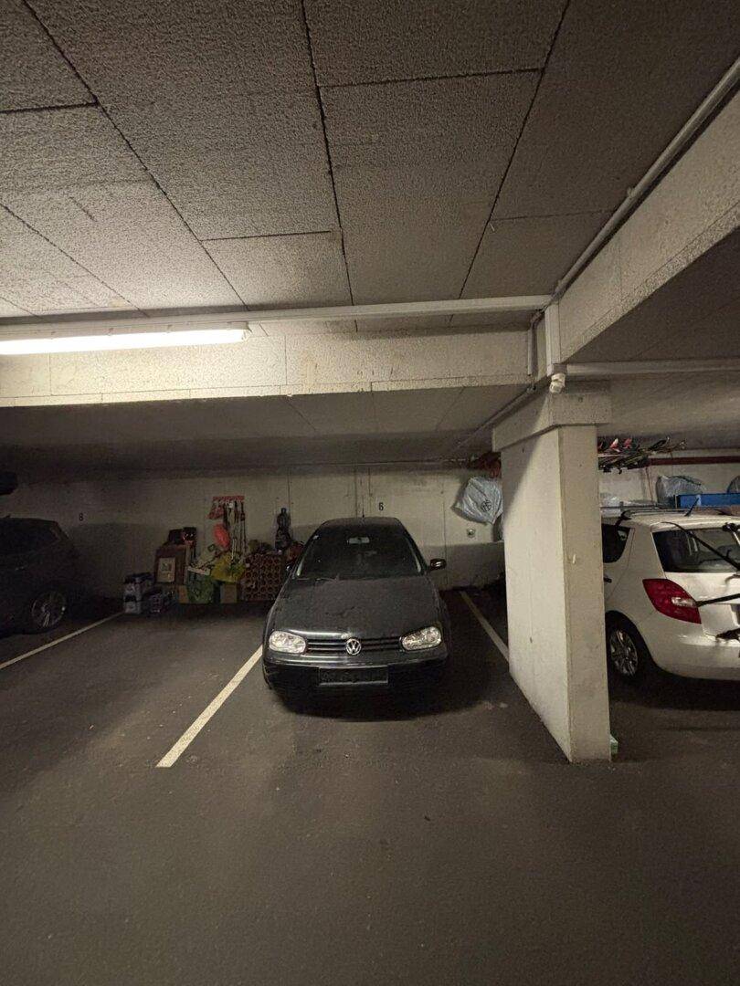Tiefgaragenstellplatz mit einem geparkten Auto, umgeben von weiteren Fahrzeugen und Lagerbereichen.