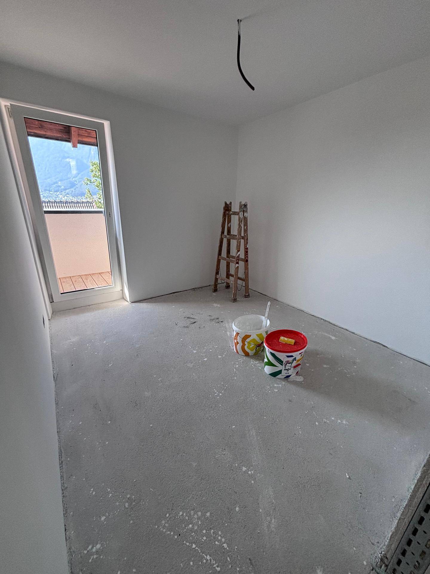 Rohbauzimmer mit weißer Grundierung, Betonboden und Balkontür, bereit für den Ausbau.