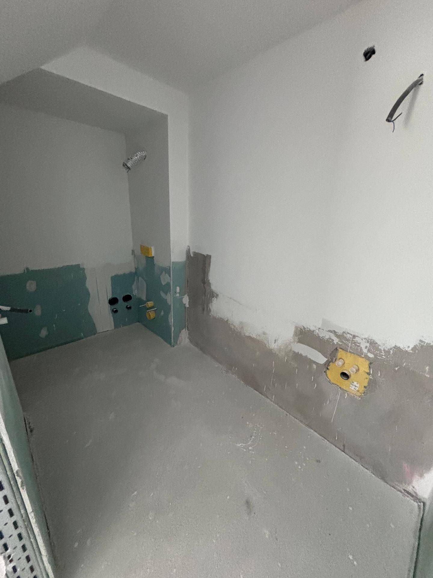 Rohbau-Badezimmer mit sichtbaren Installationen und vorbereiteten Wänden für Fliesen.