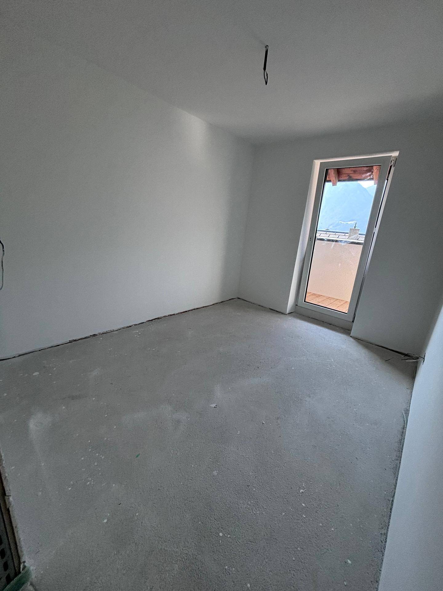 Unfertiger Raum mit weiß gestrichenen Wänden und Zugang zu einem kleinen Balkon.