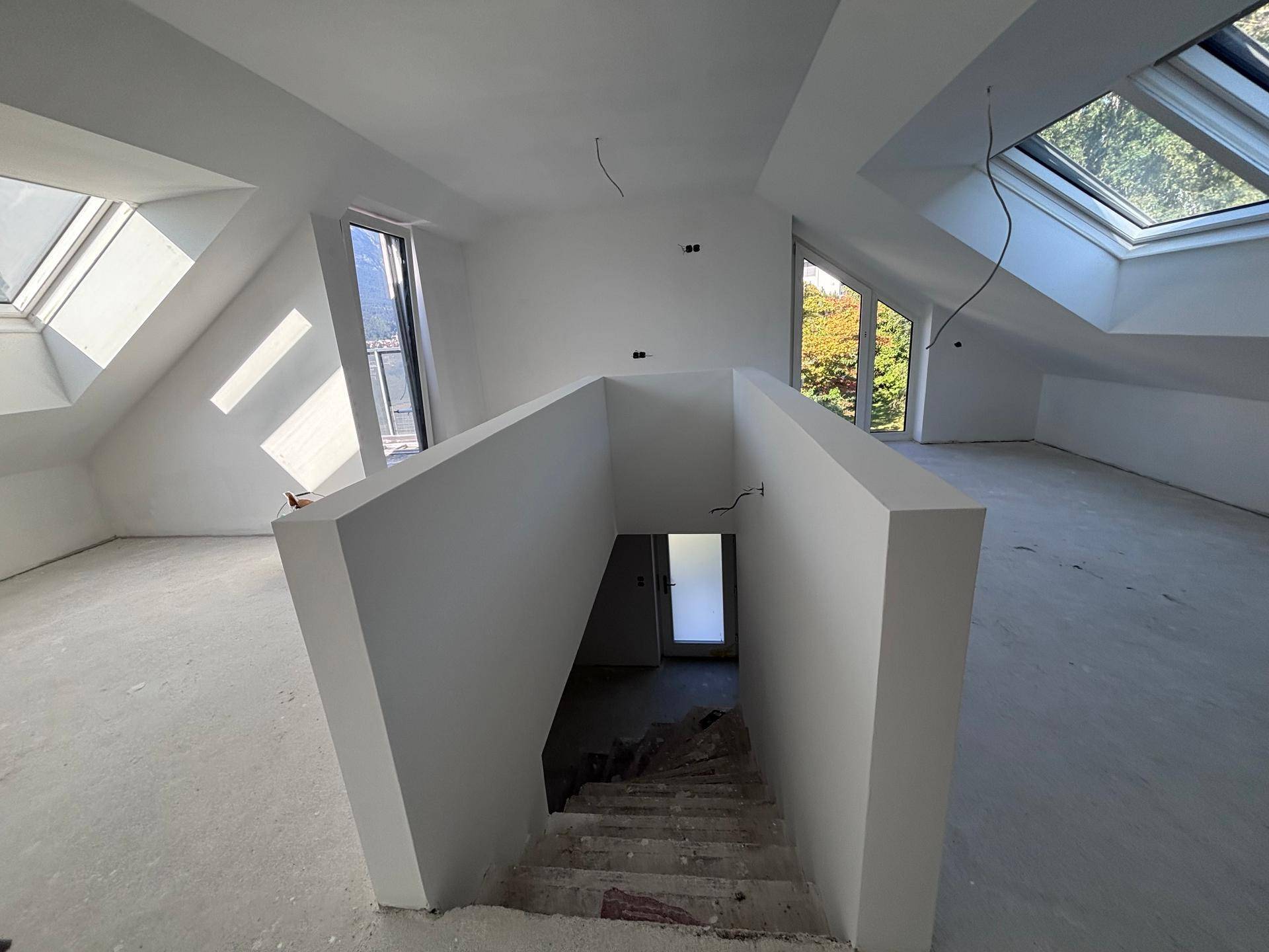 Heller Dachbodenraum im Rohbau mit großen Dachfenstern und Treppenabgang.