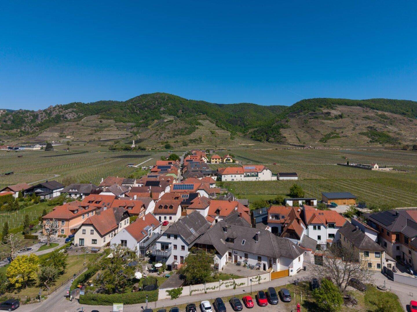 Luftaufnahme eines malerischen Dorfes umgeben von weitläufigen Weinbergen und grünen Hügeln.